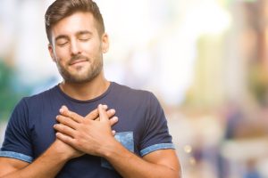 Young handsome man over isolated background smiling with hands on chest with closed eyes and grateful gesture on face. Health concept.